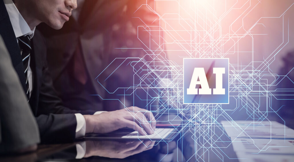ノートパソコンを操作するスーツ姿の人と、手元に浮かぶ「AI」の文字